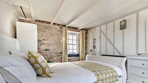 A bedroom with a white bed, a stone wall, a window, and a white dresser. - 3 Bed in St. Austell (oc-83541) (Gorran Haven)