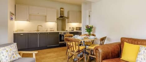 A modern kitchen with dark cabinets, a dining table with chairs, and a leather sofa with a yellow pillow.