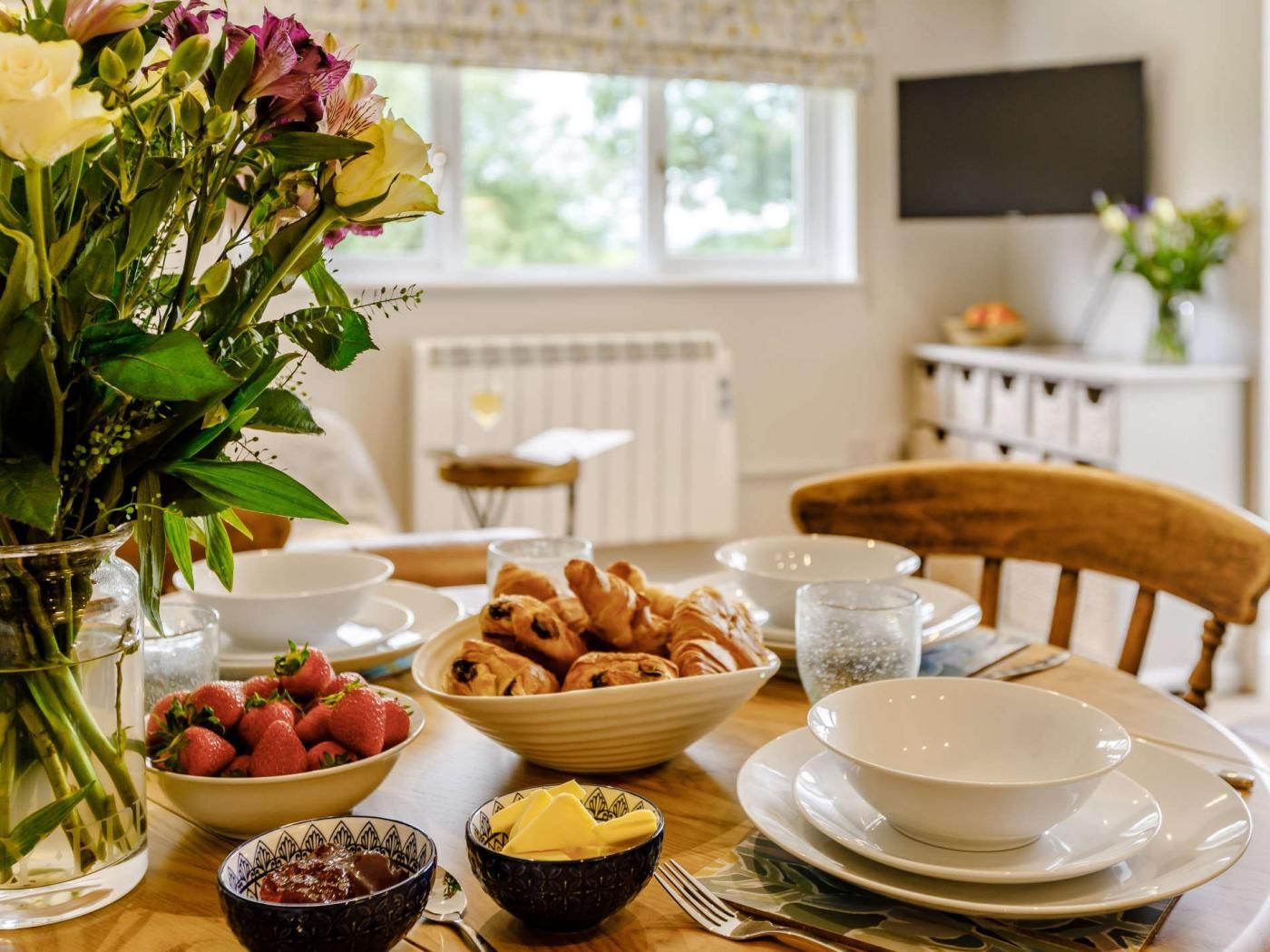 Une table à manger avec des aliments pour le petit-déjeuner, un vase de fleurs et une vue sur une fenêtre avec un radiateur.