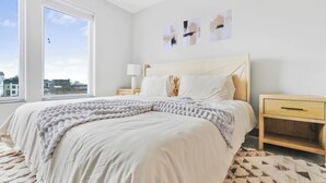 Um quarto com uma cama grande, uma mesa de cabeceira, uma luminária e obras de arte na parede.