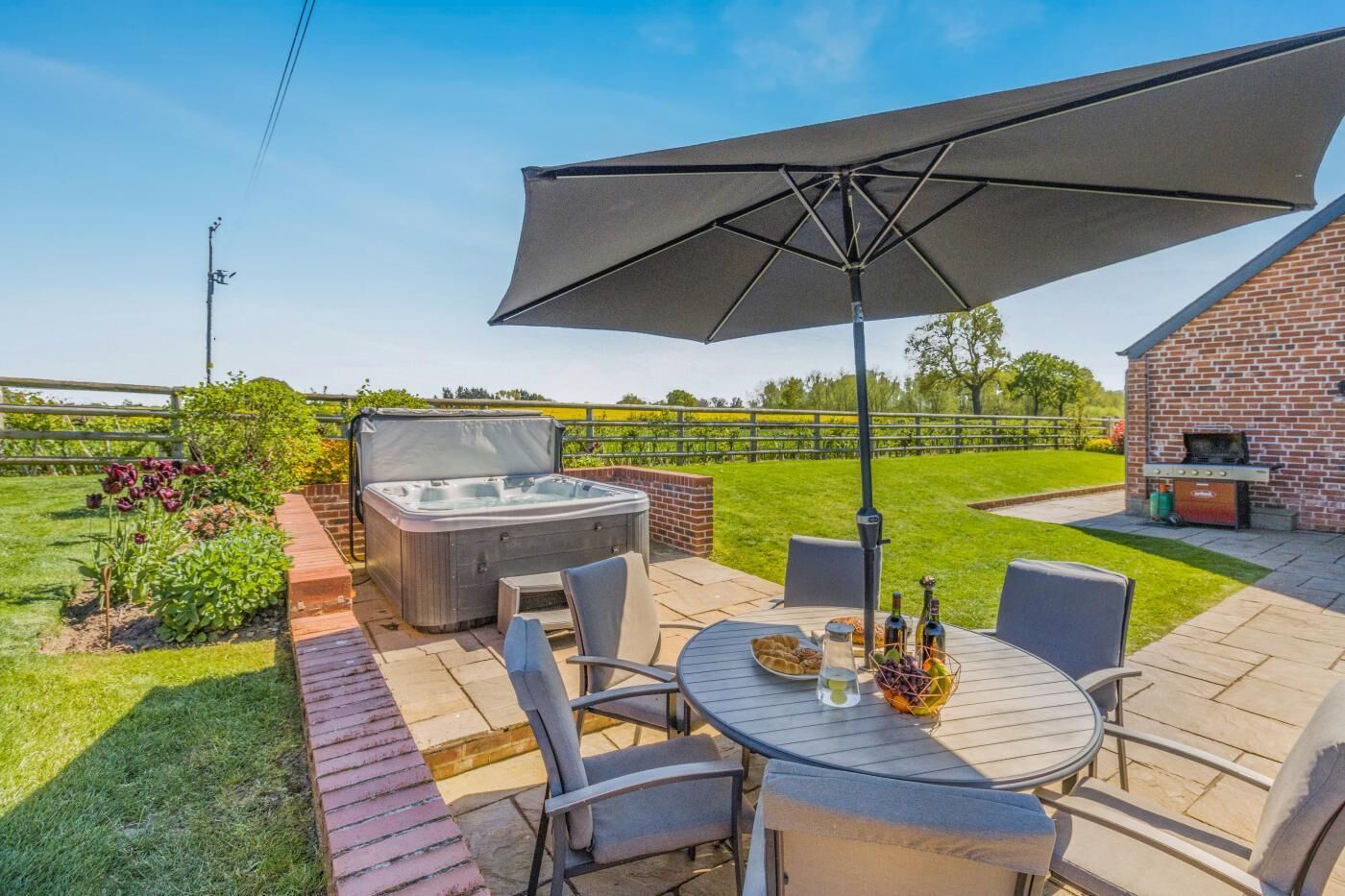 Un patio exterior con un jacuzzi, una mesa con sillas y una parrilla.