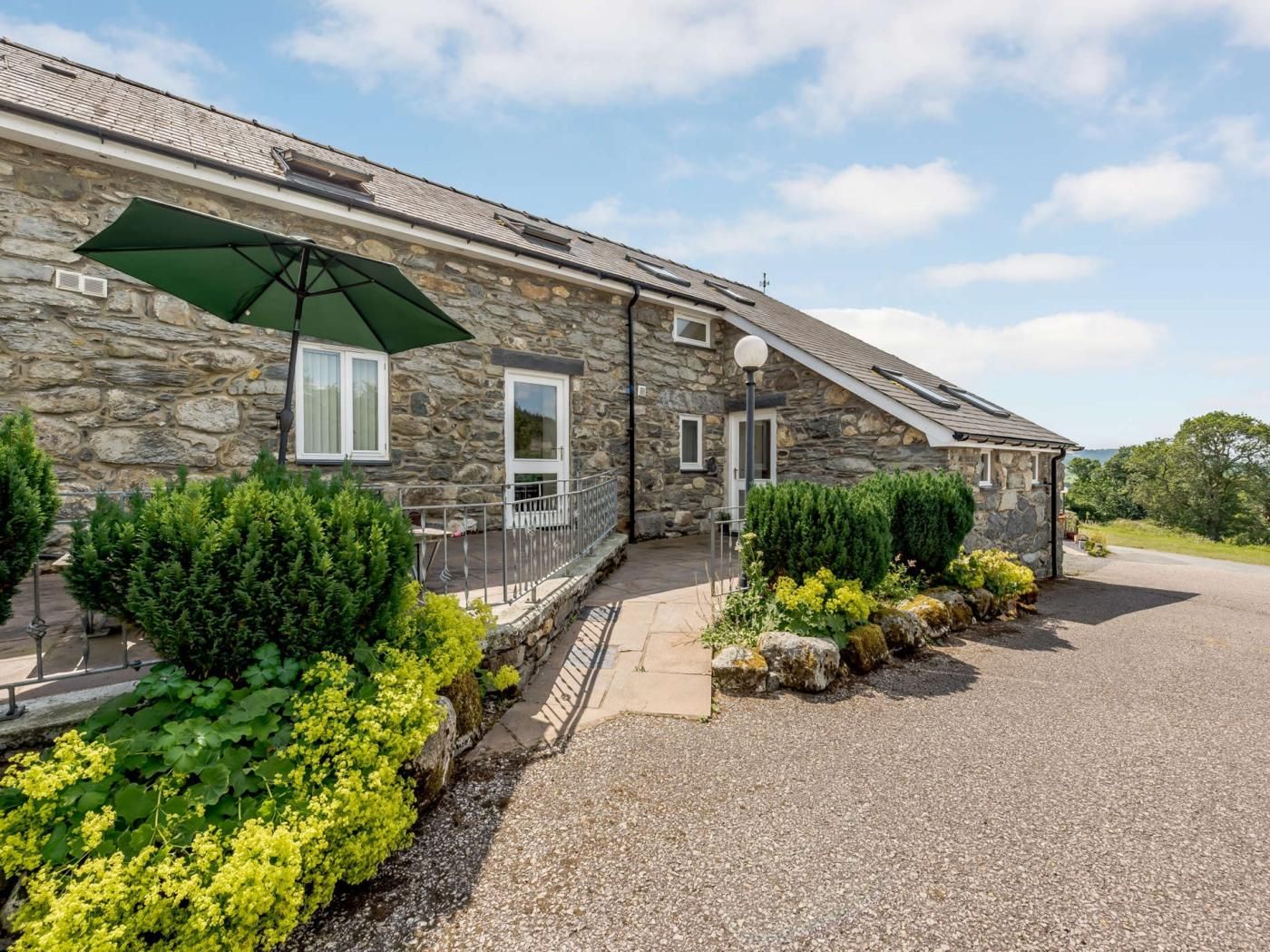 A stone building with a covered porch, a gravel driveway, and a view of the surrounding landscape.