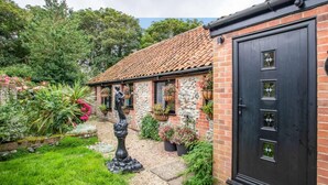 Ein Ziegelhaus mit einem Ziegeldach, eine schwarze Tür mit Fensterfeldern und ein Garten mit verschiedenen Pflanzen und einer Statue.
