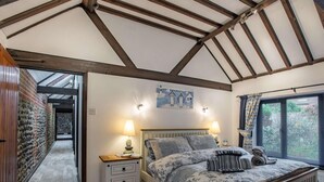 Ein Schlafzimmer mit Holzboden, einem Bett mit gemusterten Betttextilien, einem Nachttisch mit Lampe und einem Fenster mit Vorhängen.