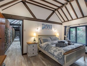 A bedroom with a wooden ceiling, a bed with patterned bedding, a nightstand with a lamp, and a window with curtains. - 3 Bed in Norwich (oc-83711) (Trimingham)