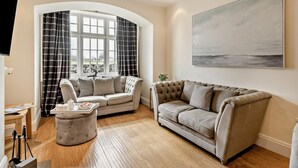 Uma sala de estar com um sofá, um banquinho e um quadro na parede.