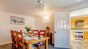 A dining room with a wooden table, chairs, a vase of flowers, and a candle. - 3 Bed in Crewkerne (oc-83943) (Haselbury Plucknett)