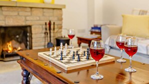 A chessboard on a wooden table with glasses of red wine, a fireplace, and a sofa in the background. - 3 Bed in Crewkerne (oc-83943) (Haselbury Plucknett)