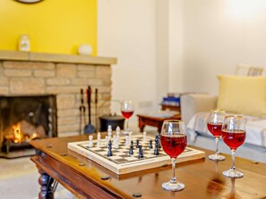 A chessboard on a wooden table with glasses of red wine, a fireplace, and a sofa in the background. - 3 Bed in Crewkerne (oc-83943) (Haselbury Plucknett)