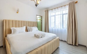 Quarto de hotel com uma cama grande, uma porta verde e uma janela com cortinas.