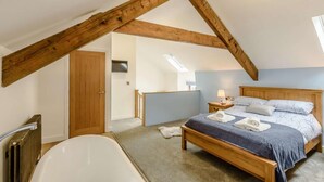 Een slaapkamer met een houten plafond, een bed met een blauwe deken, een wit bad en een houten deur.