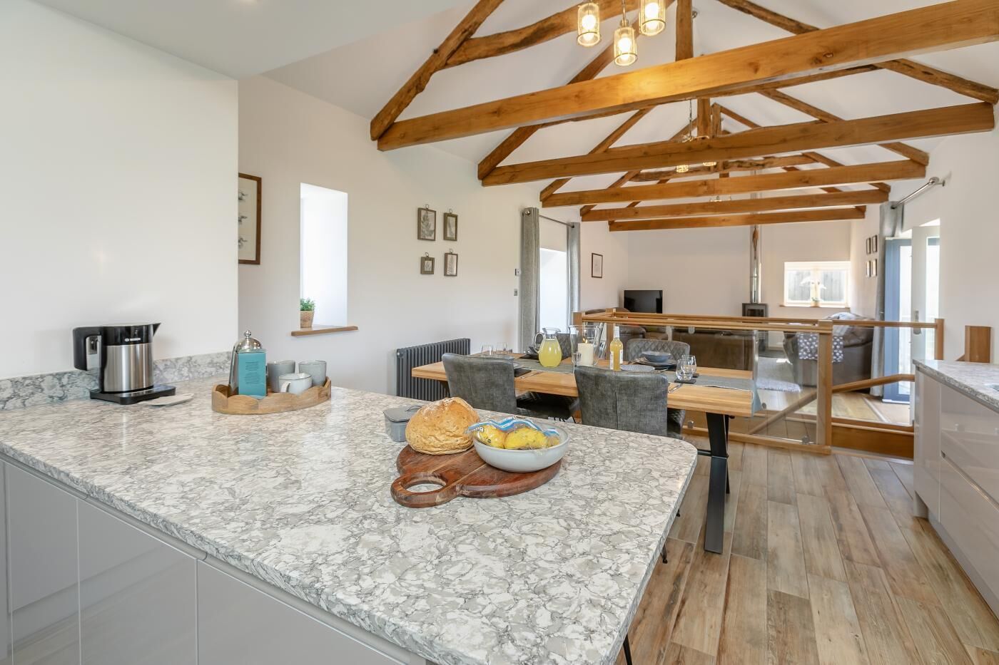 Een keuken met marmeren aanrechtbladen, houten balken en een eethoek met een tafel en stoelen.
