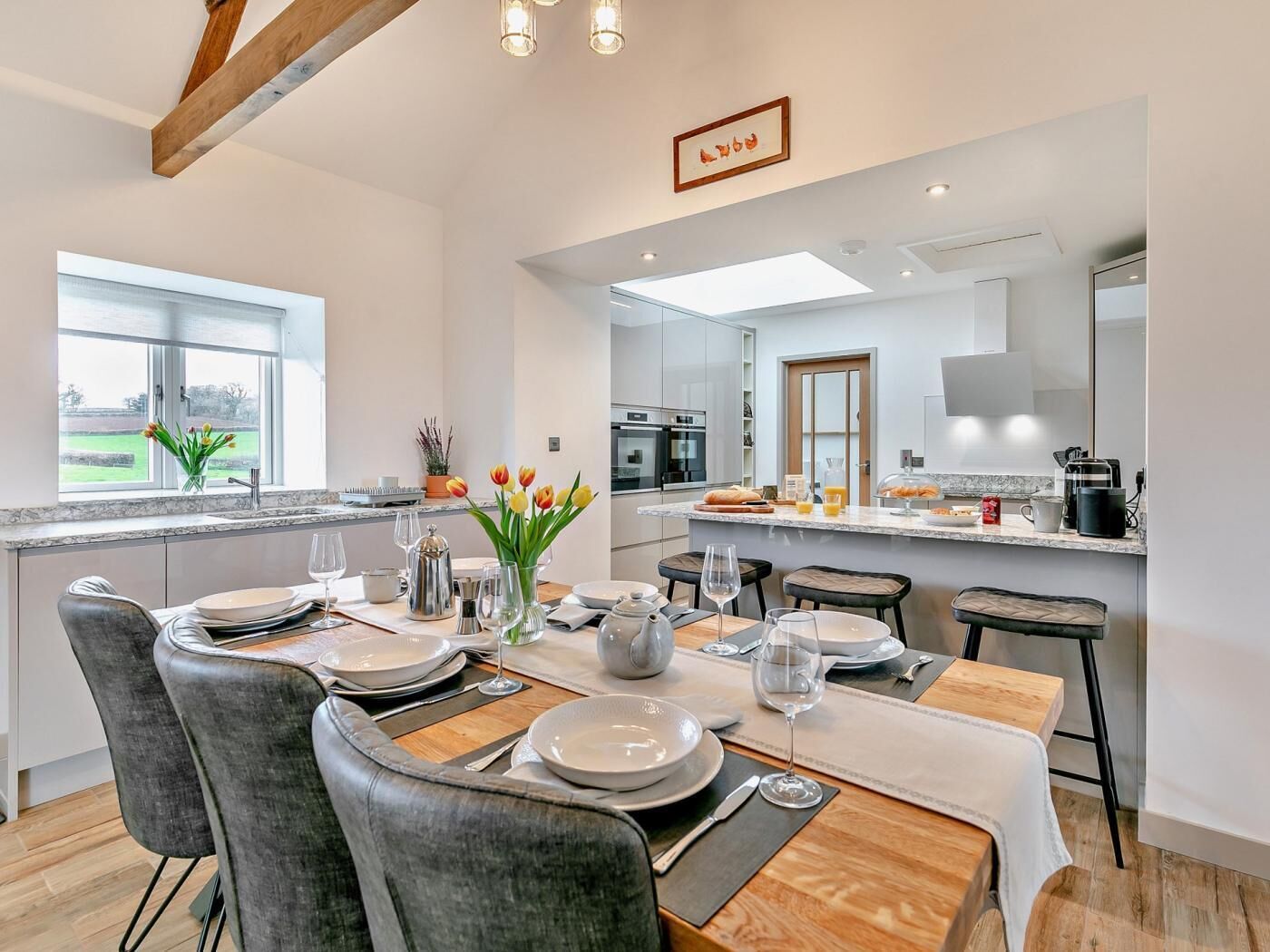 A modern kitchen with a dining area, featuring a large island, bar stools, and a view of the outdoors.