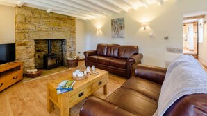 A cozy living room with a stone fireplace, leather sofa, wooden coffee table, and a television on a wooden stand. - 3 Bed in Wrexham (oc-83938) (Coedpoeth)