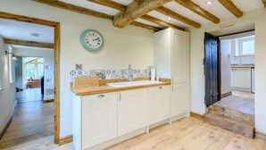 A kitchen with wooden beams, a clock, white cabinets, and a tiled backsplash. - 3 Bed in Wrexham (oc-83938) (Coedpoeth)