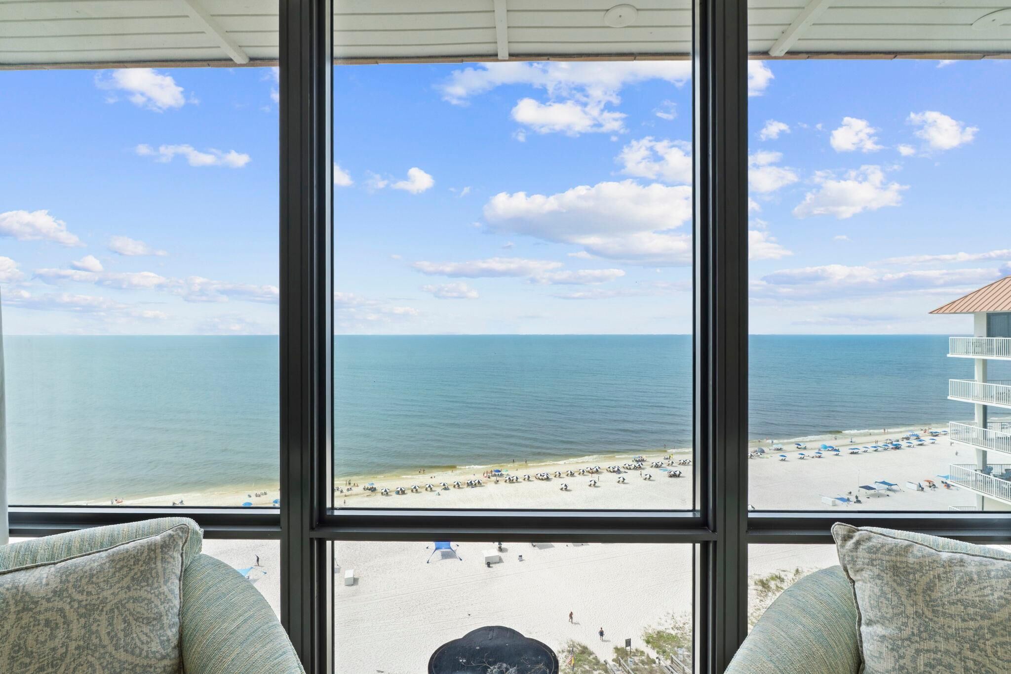 A view from a window overlooking a beach with a clear sky and calm sea.