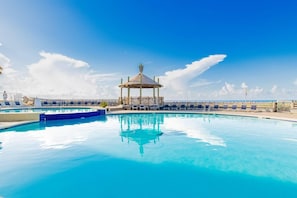 Ein klares, blaues Schwimmbecken mit Liegestühlen, einer Laube und Blick auf den Ozean.