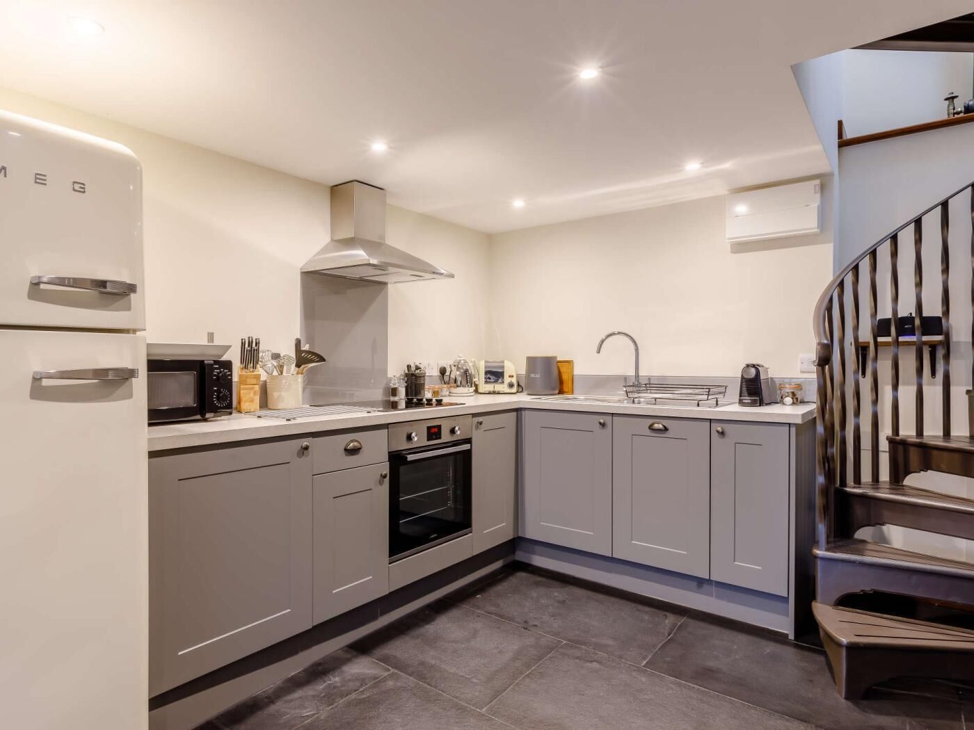 A modern kitchen with grey cabinets, a built-in oven, a microwave, and a stainless steel range hood.