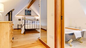 A bedroom with a wooden dresser, a bed with a metal frame, a wooden ceiling beam, and a bathroom with a bathtub. - 1 Bed in Frome (oc-83834) (Holwell)