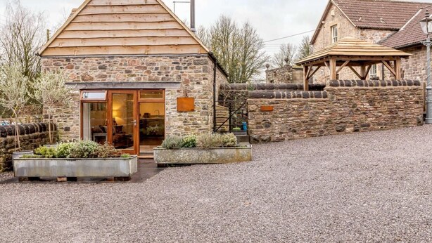A stone building with a wooden gable roof, a glass door entrance, and a gravel driveway. - 1 Bed in Frome (oc-83834) (Holwell)
