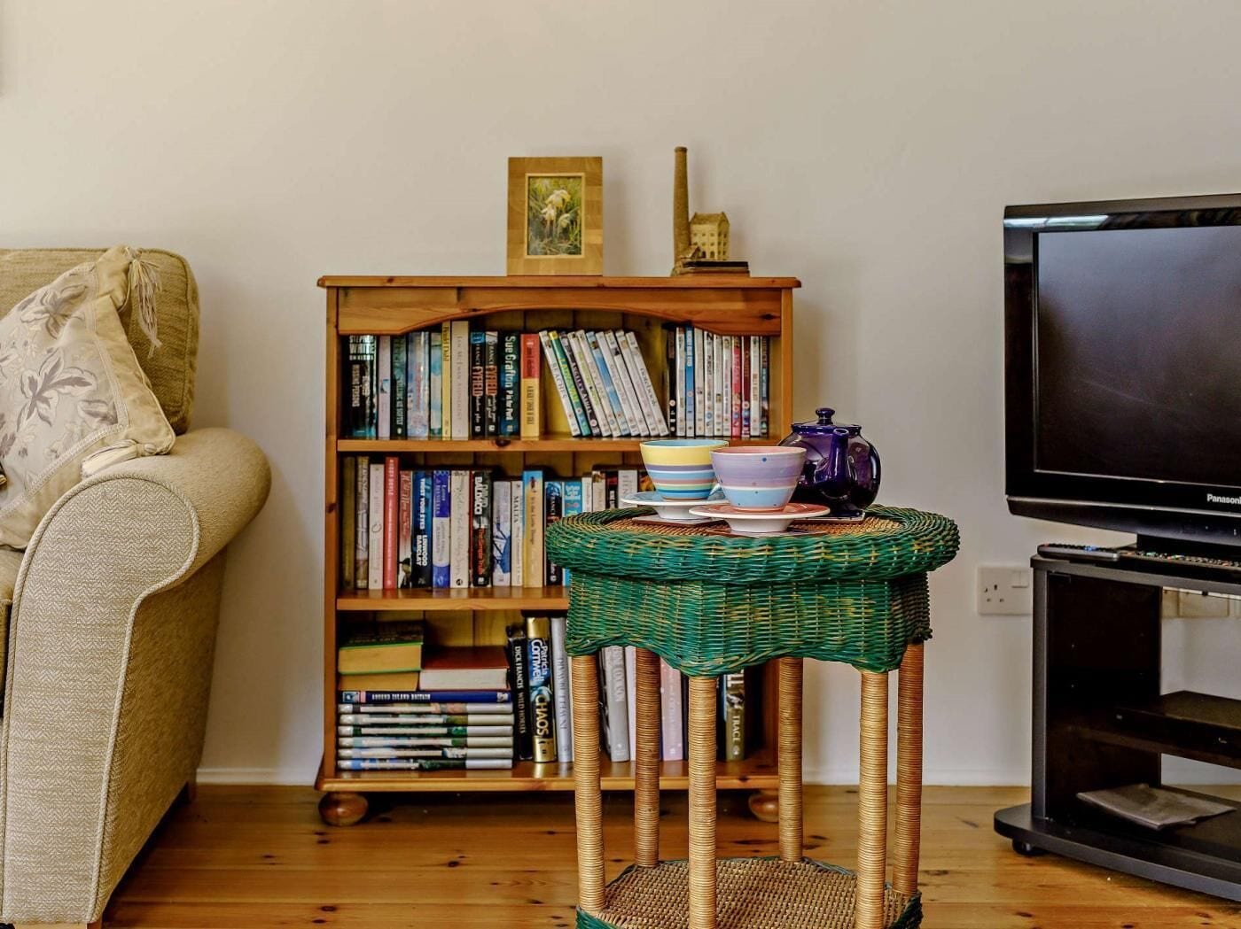 A living room with a sofa, a bookshelf, a small table with a teapot, and a television.