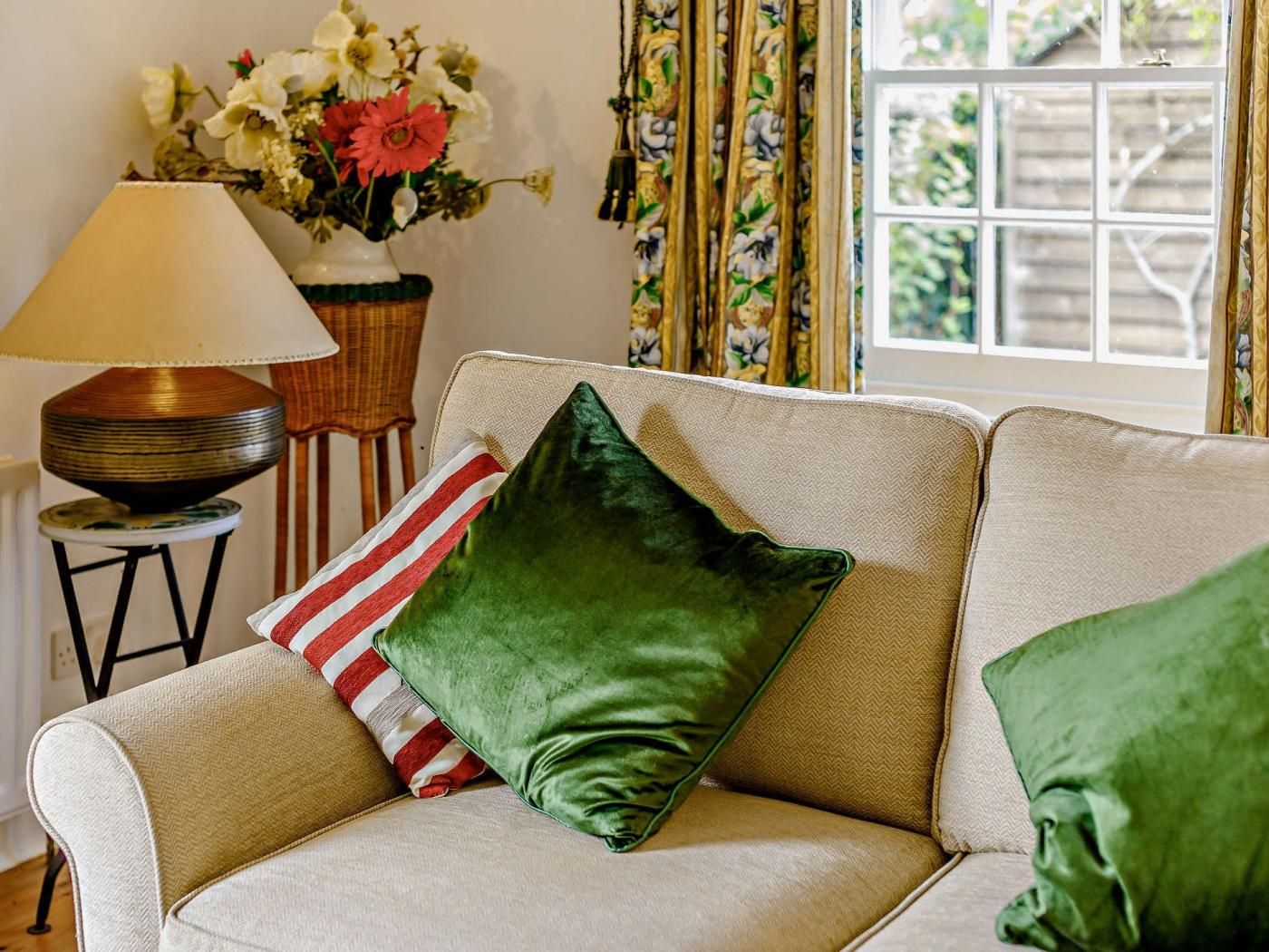 A sofa with green and striped pillows, a lamp, and a floral arrangement.