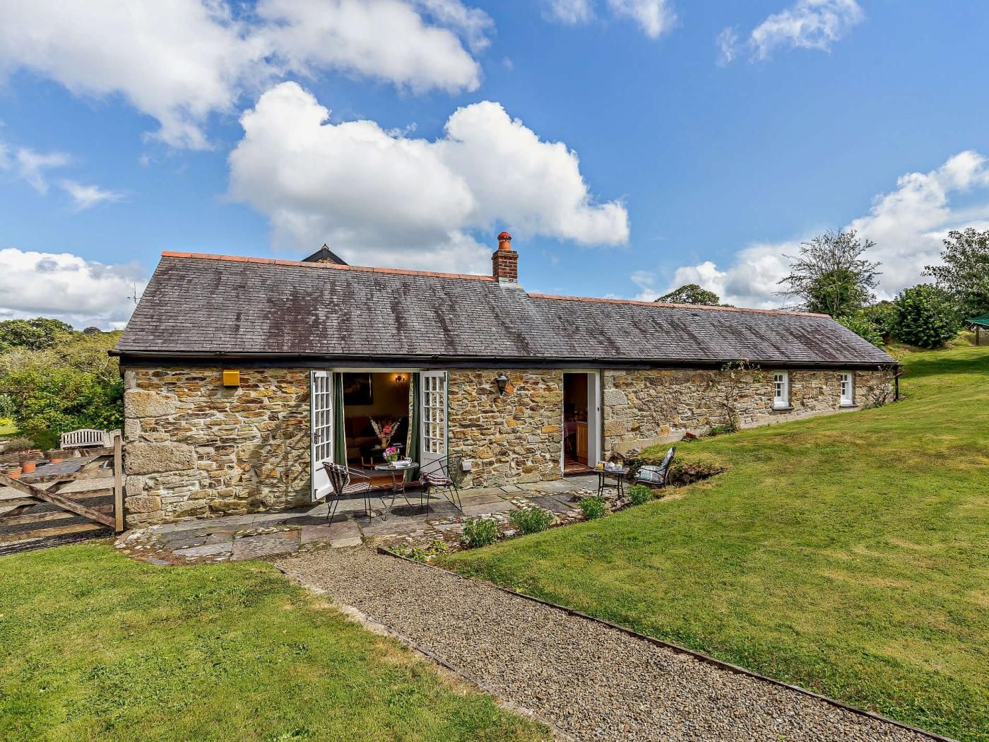 A stone cottage with a sloped roof, a chimney, and a small porch with outdoor seating.