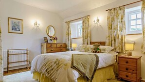 Een slaapkamer met een groot bed, een kaptafel, een spiegel en een nachtkastje met een lamp.