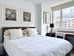 A neatly made bed with white bedding, a bedside table with a lamp, and two framed abstract paintings on the wall. - Nomad Luxury Pied-a-Terre NYC (NY)