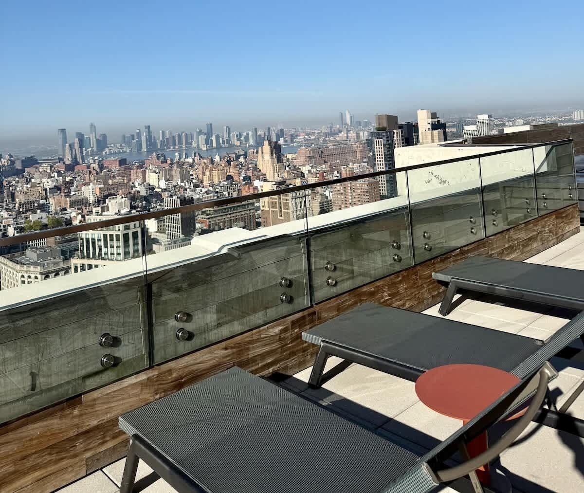 Een terras op het dak met uitzicht over de stad, glazen hekwerk en loungestoelen.