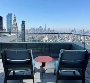Eine Dachterrasse mit zwei Stühlen und einem kleinen Tisch, mit Blick auf die Stadt.