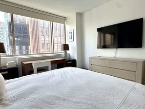A hotel room with a large bed, a desk, a chair, a dresser, a TV, and a window with a city view. - Pied-a-terre in the Sky (NY)