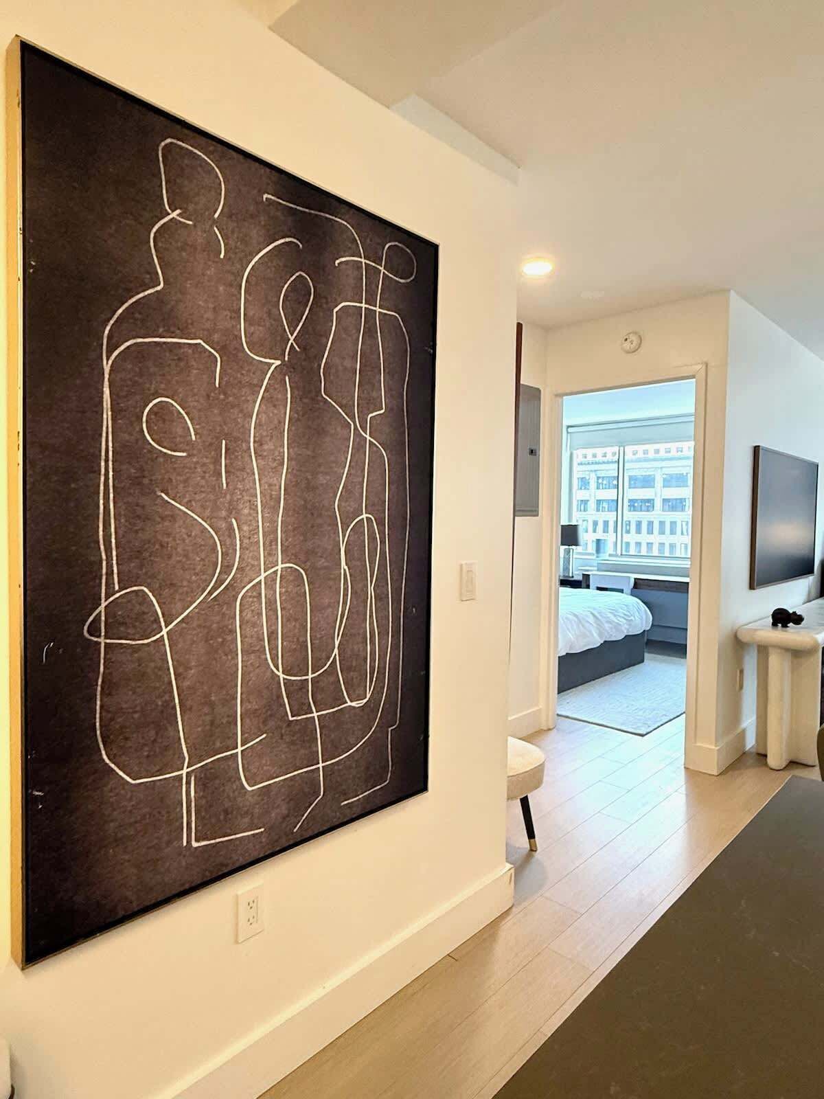 Ein modernes Interieur mit einem großen abstrakten Kunstwerk an der Wand, ein sichtbares Schlafzimmer mit Bett und Fernseher sowie ein Flur, der zu einem weiteren Raum führt.