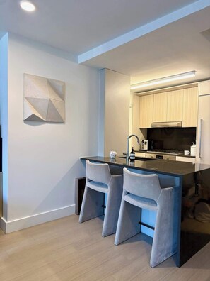 A modern kitchen with a central island, bar stools, and a geometric wall art piece. - Nomad Luxury Pied-a-Terre NYC (NY)
