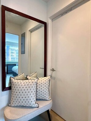 A hallway with a mirror, a door, and a bench with patterned cushions. - Pied-a-terre in the Sky (NY)