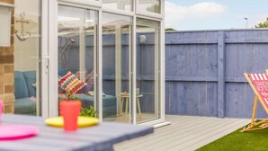 Une terrasse avec une table, une clôture bleue et une porte vitrée donnant sur une pièce.