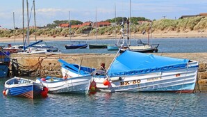 Un port où sont amarrés plusieurs bateaux, une plage de sable et des maisons en arrière-plan.