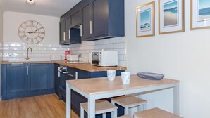 Une cuisine moderne avec des meubles de couleur sombre, un plan de travail en bois, un évier blanc, une horloge et des tableaux encadrés accrochés au mur.