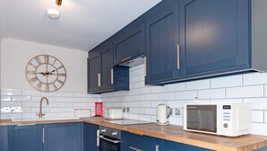 Une cuisine moderne avec des meubles de couleur bleu foncé, un plan de travail en bois, un four à micro-ondes blanc, un grille-pain et une horloge.