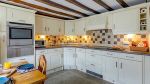 A kitchen with white cabinets, a microwave, an oven, and a checkered backsplash. - 2 Bed in Bideford (oc-83808) (Weare Giffard)