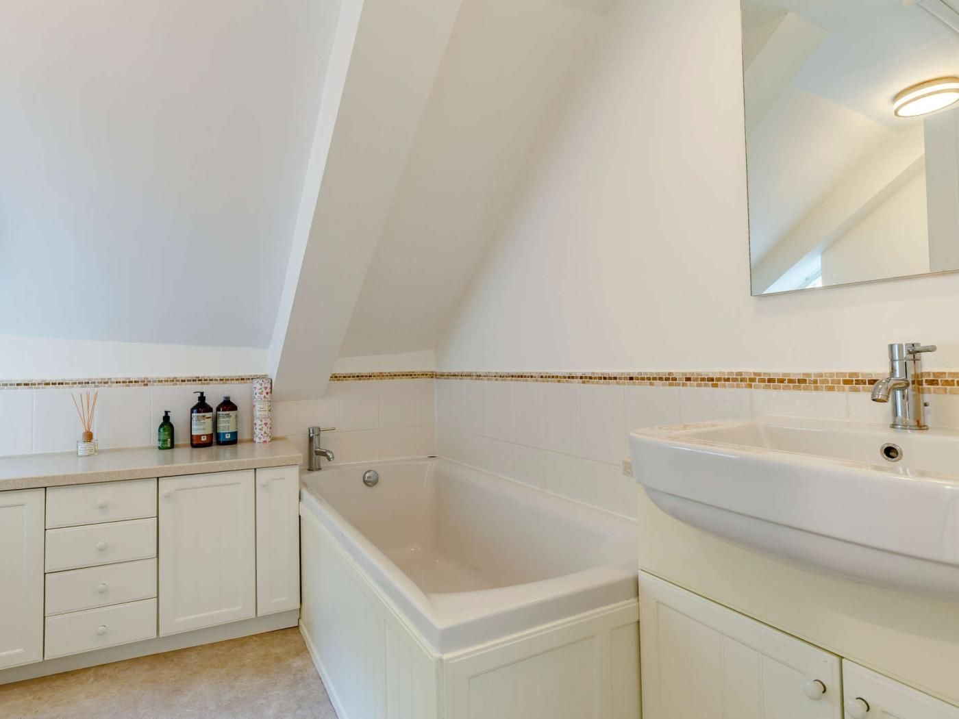 Un bagno con una vasca, un lavandino e uno specchio. Sono presenti articoli da toilette sul ripiano.