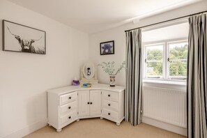 Une chambre avec une commode blanche, une fenêtre avec des rideaux et deux tableaux encadrés accrochés au mur.