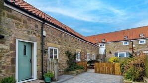 A stone building with a tiled roof, a paved courtyard, and a wooden fence. - 4 Bed in Chathill (oc-83469) (Swinhoe)