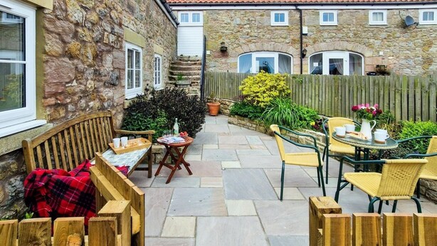 A stone building with a tiled roof, outdoor seating with chairs and tables, and a wooden fence. - 4 Bed in Chathill (oc-83469) (Swinhoe)