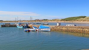 A calm harbor with several boats docked, a stone breakwater, and a sandy beach in the background. - 4 Bed in Chathill (oc-83469) (Swinhoe)