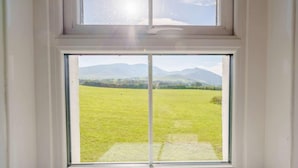 Una ventana con vistas a un campo verde y montañas distantes.