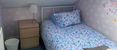 A bedroom with a skylight, a bed with floral bedding, a bedside table with a lamp, and a radiator.