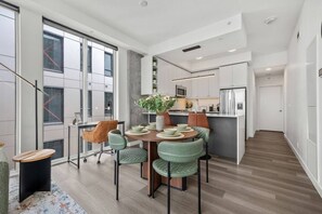A modern kitchen with white cabinets, a stainless steel refrigerator, and a dining area with a round table and chairs.