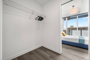 A room with a bed, a window with a view, a hanging rack, and a door leading to another room.