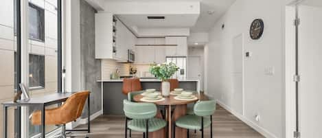 Une cuisine moderne avec des meubles blancs, un îlot central et un coin repas comprenant une table ronde et quatre chaises.